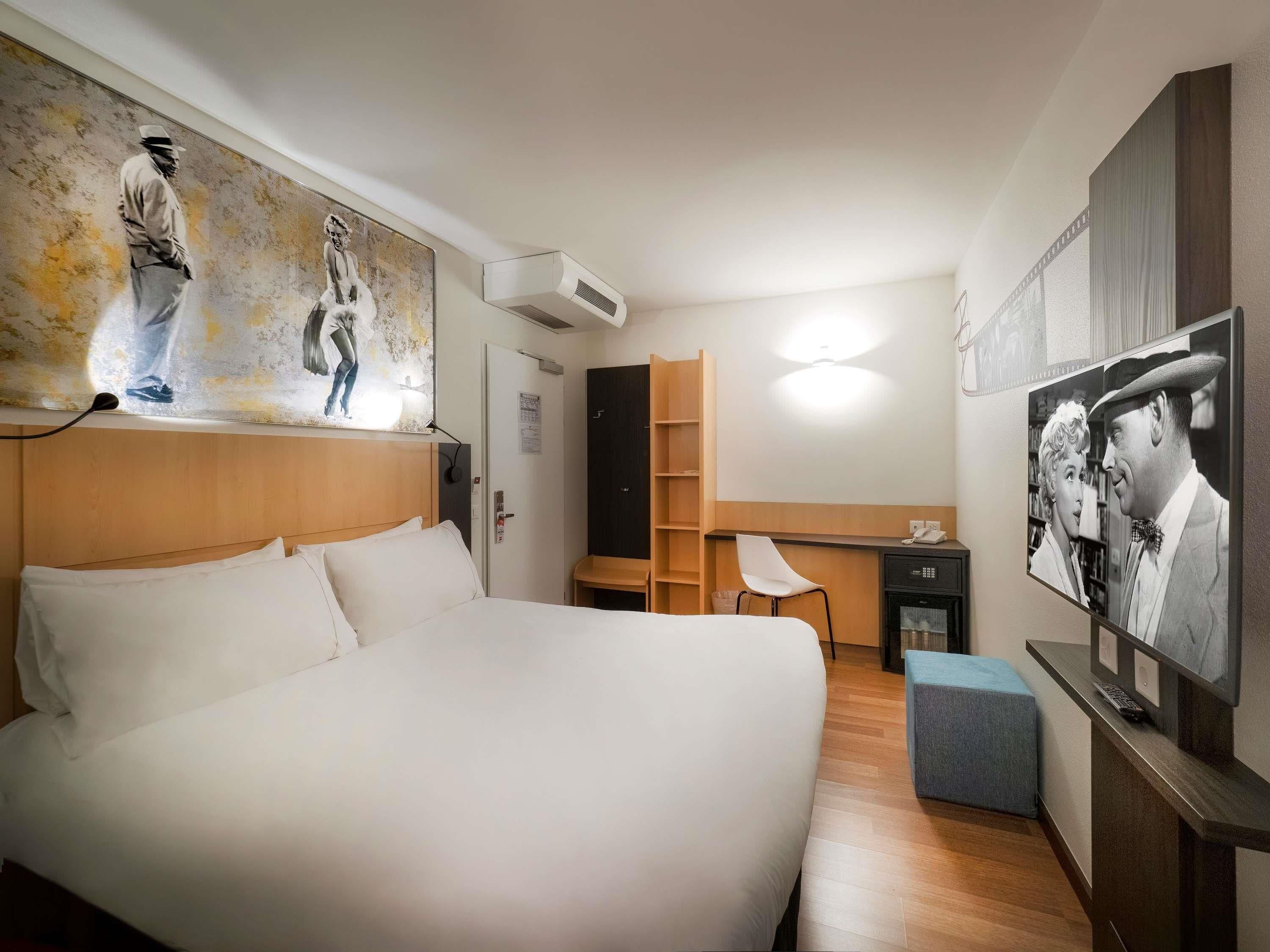 A hotel room with a large bed, a desk, a chair, and artwork on the walls.