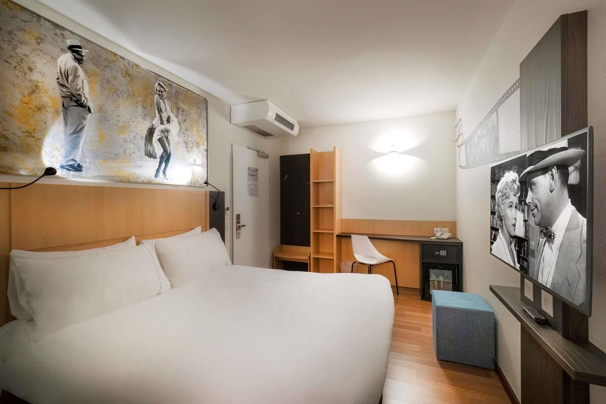 Una habitación de hotel con una cama grande, un escritorio, una silla y obras de arte en las paredes.