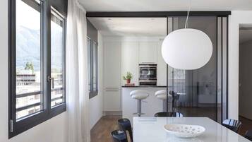 A modern kitchen with white cabinets, a large window, and a dining area with a white table and chairs.