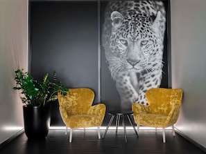 Un interior moderno con dos sillones de terciopelo, una planta en maceta y una obra de arte grande con estampado de leopardo en la pared.