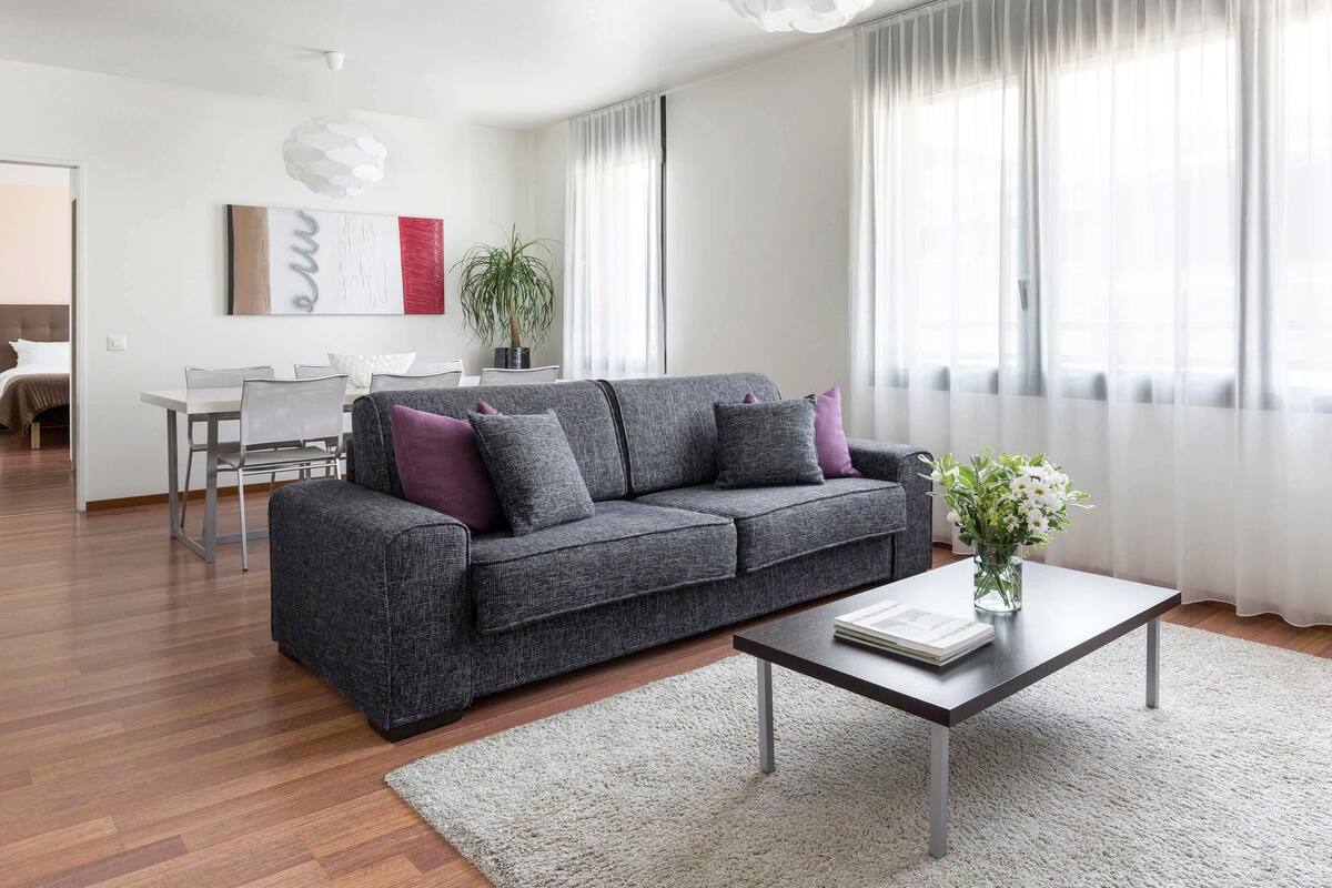 Una sala de estar moderna con un sofá gris, una mesa de centro y un comedor al fondo.