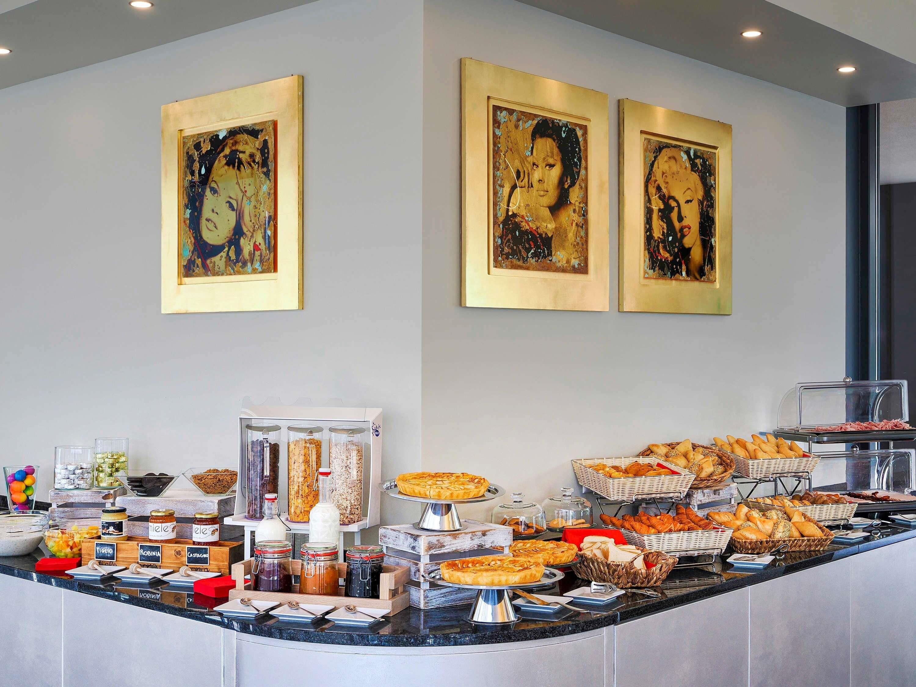Un bufé con diversos alimentos, incluyendo pasteles y pan, y tres obras de arte enmarcadas en la pared.