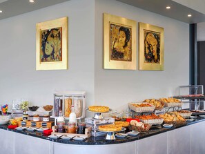 A buffet with various food items, including pastries and bread, and three framed artworks on the wall. - ibis Locarno (Locarno)