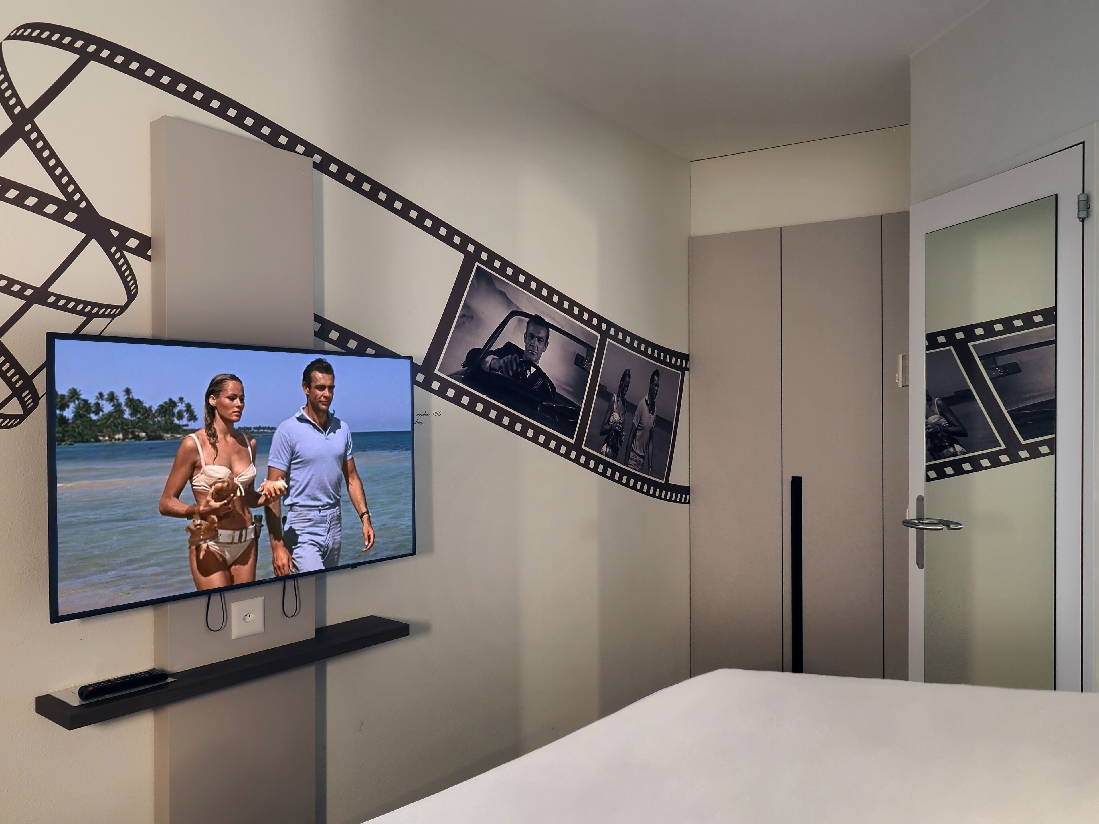 A bedroom with a television mounted on the wall, a bed, and a wardrobe.