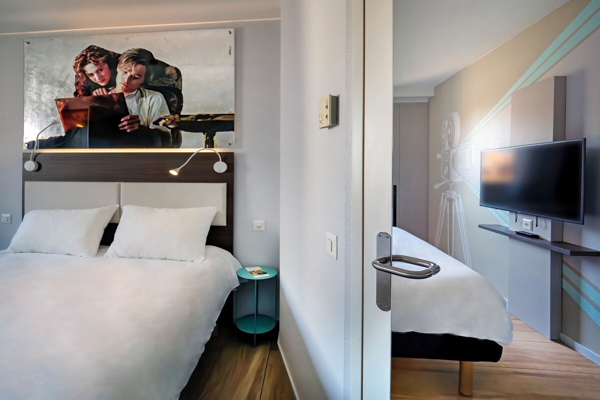 Habitació d'hotel moderna amb llit, taula de nit i televisió penjada a la paret.