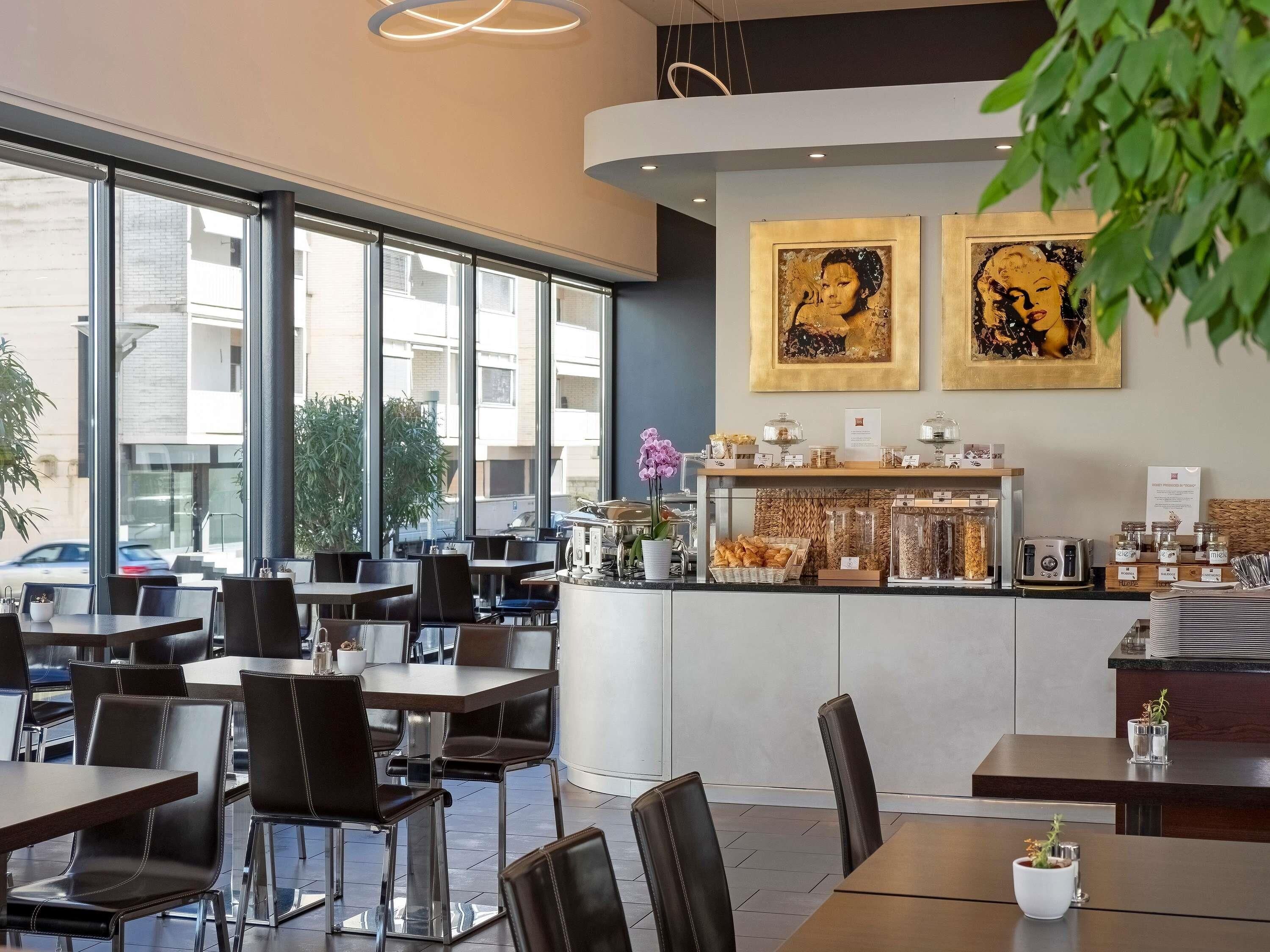 Een modern café met grote ramen, een toonbank vol gebak en twee ingelijste kunstwerken aan de muur.