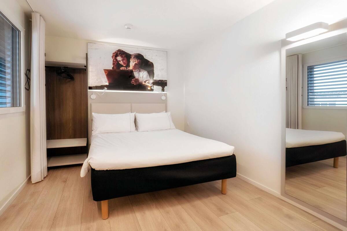 Un dormitorio con cama, armario, espejo y un cuadro colgado en la pared.