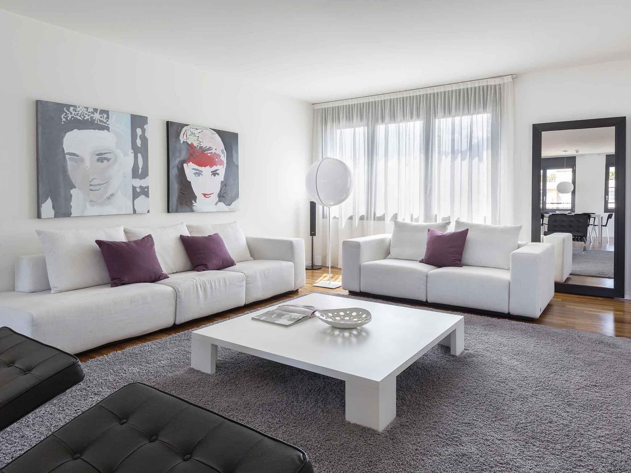 A modern living room with two white sofas, a coffee table, and artwork on the wall.