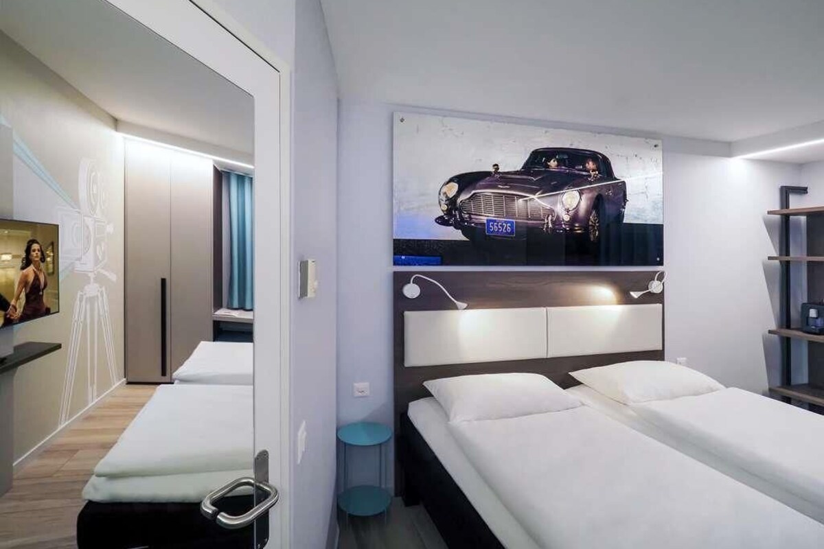Habitació d'hotel moderna amb un llit gran, una taula de nit, un televisor fixat a la paret i un quadre amb una foto d'un cotxe.