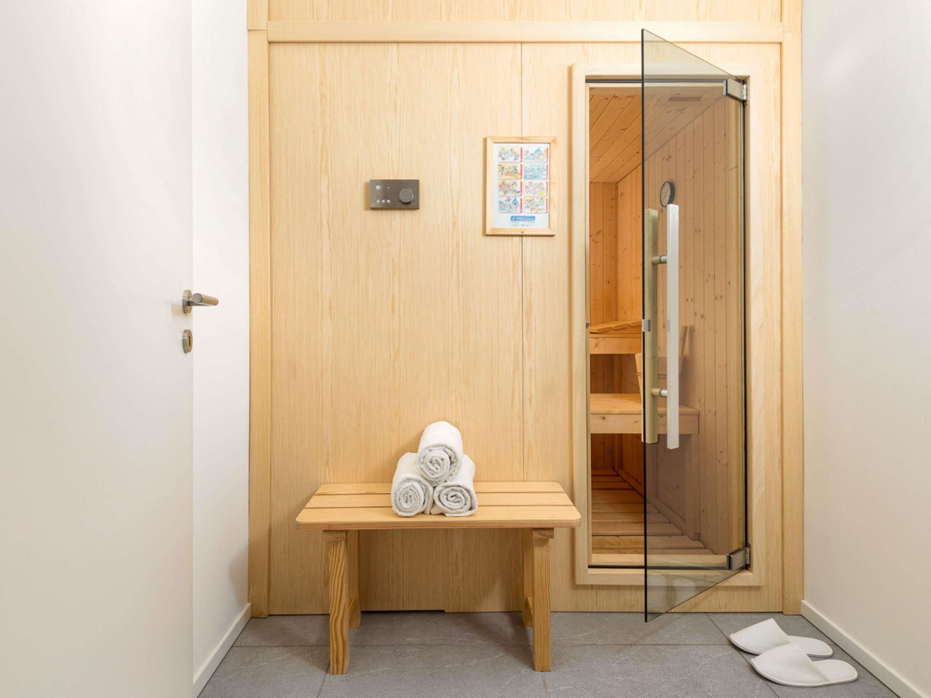 A wooden door with a small table holding rolled towels, a glass door leading to a shower area, and a clock on the wall.