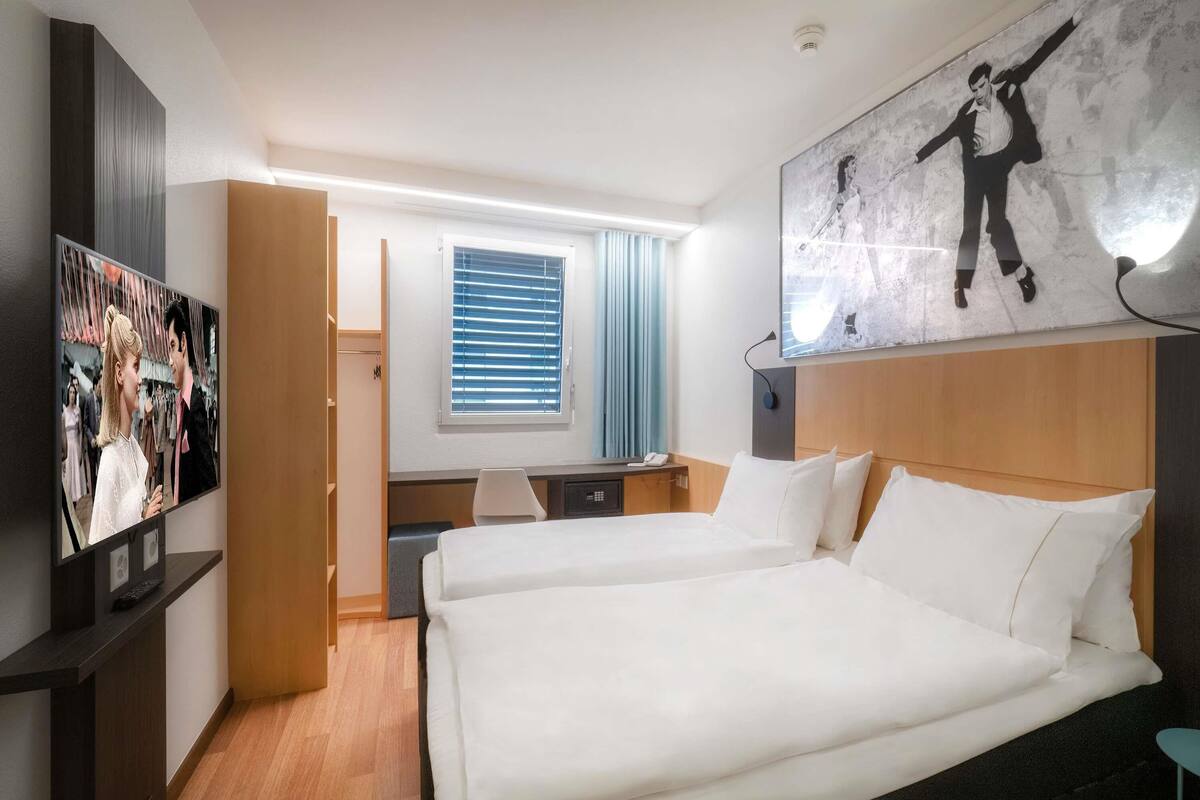 Una habitación de hotel con cama, escritorio, silla, televisor y un cuadro en la pared.