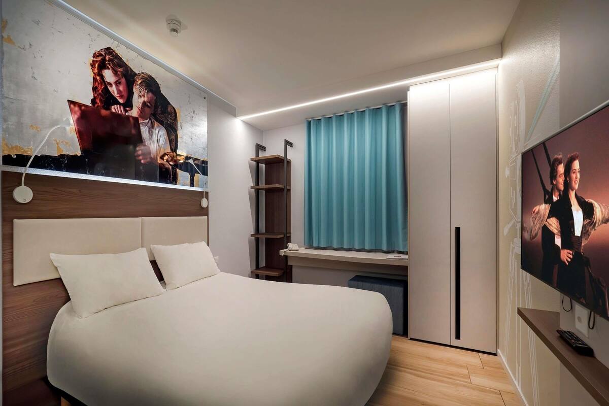 Una habitación de hotel moderna con una cama grande, un escritorio con computadora, un televisor y un cuadro en la pared.