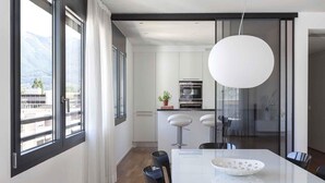 Una cocina moderna con armarios blancos, un ventanal grande y una zona de comedor con una mesa y sillas blancas.