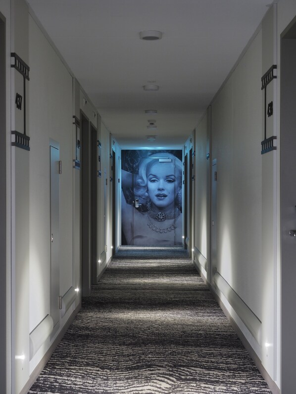 A hallway with a patterned carpet, doors on either side, and a large poster on the far wall. - ibis Locarno (Locarno)