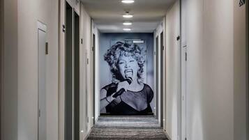 Un pasillo de hotel con alfombra estampada, puertas a ambos lados y un mural grande al final.