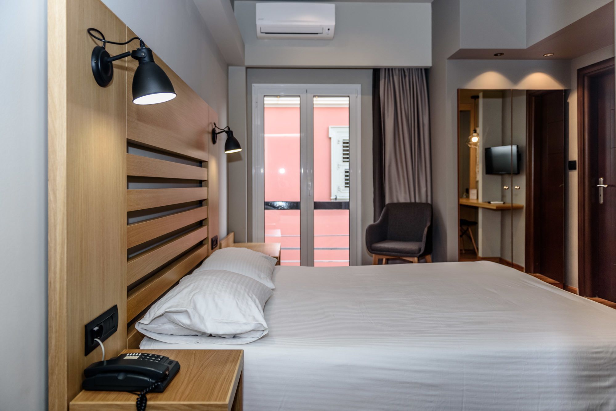 A hotel room with a bed, bedside lamp, telephone, and a view of the outside.