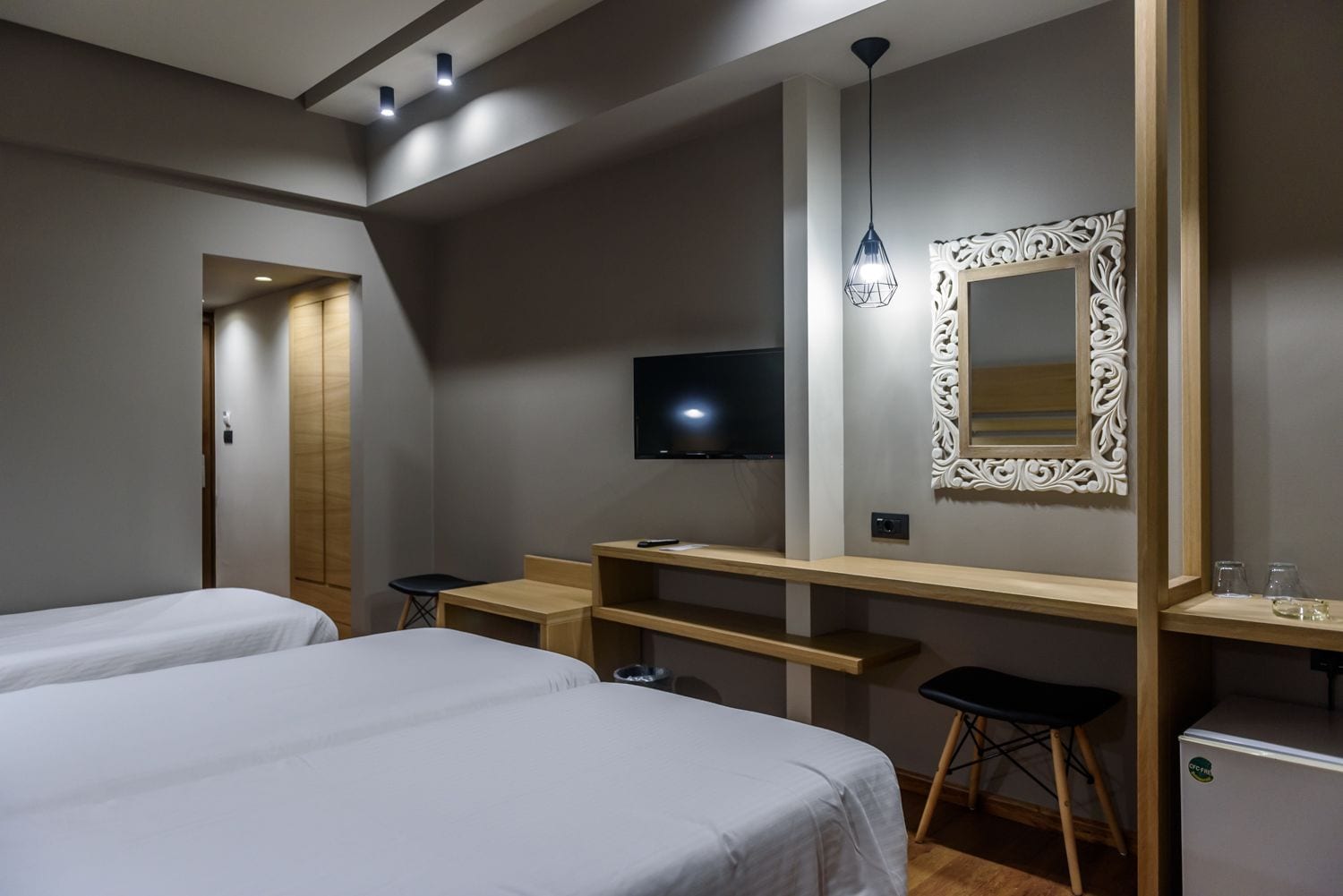 Ein Hotelzimmer mit zwei Betten, einem Schreibtisch, einem Fernseher und einem dekorativen Spiegel.