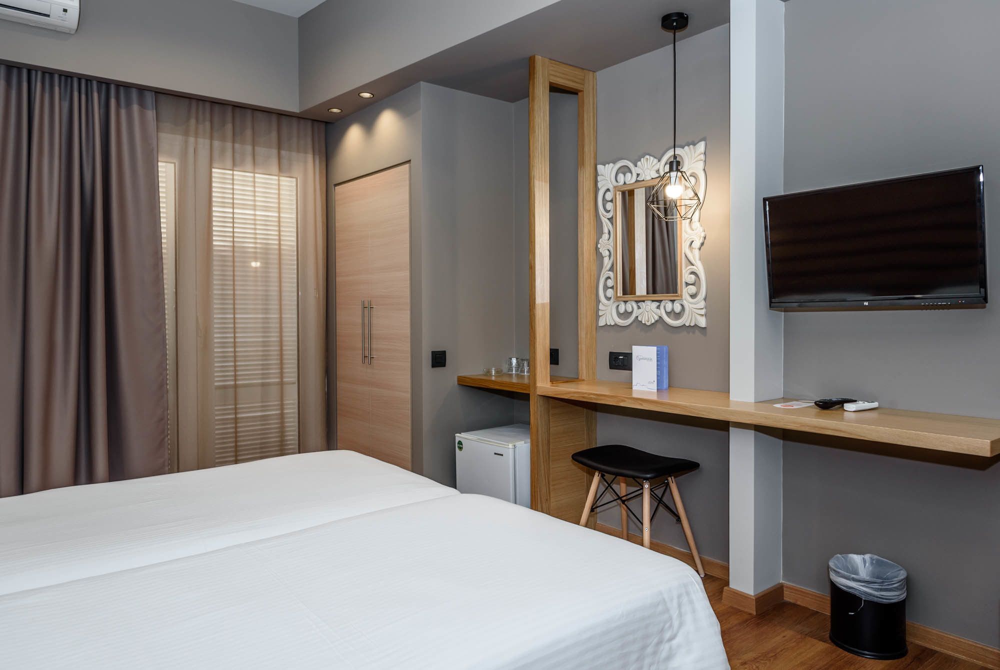 A hotel room with a bed, a desk with a mirror, a television, and a small refrigerator.
