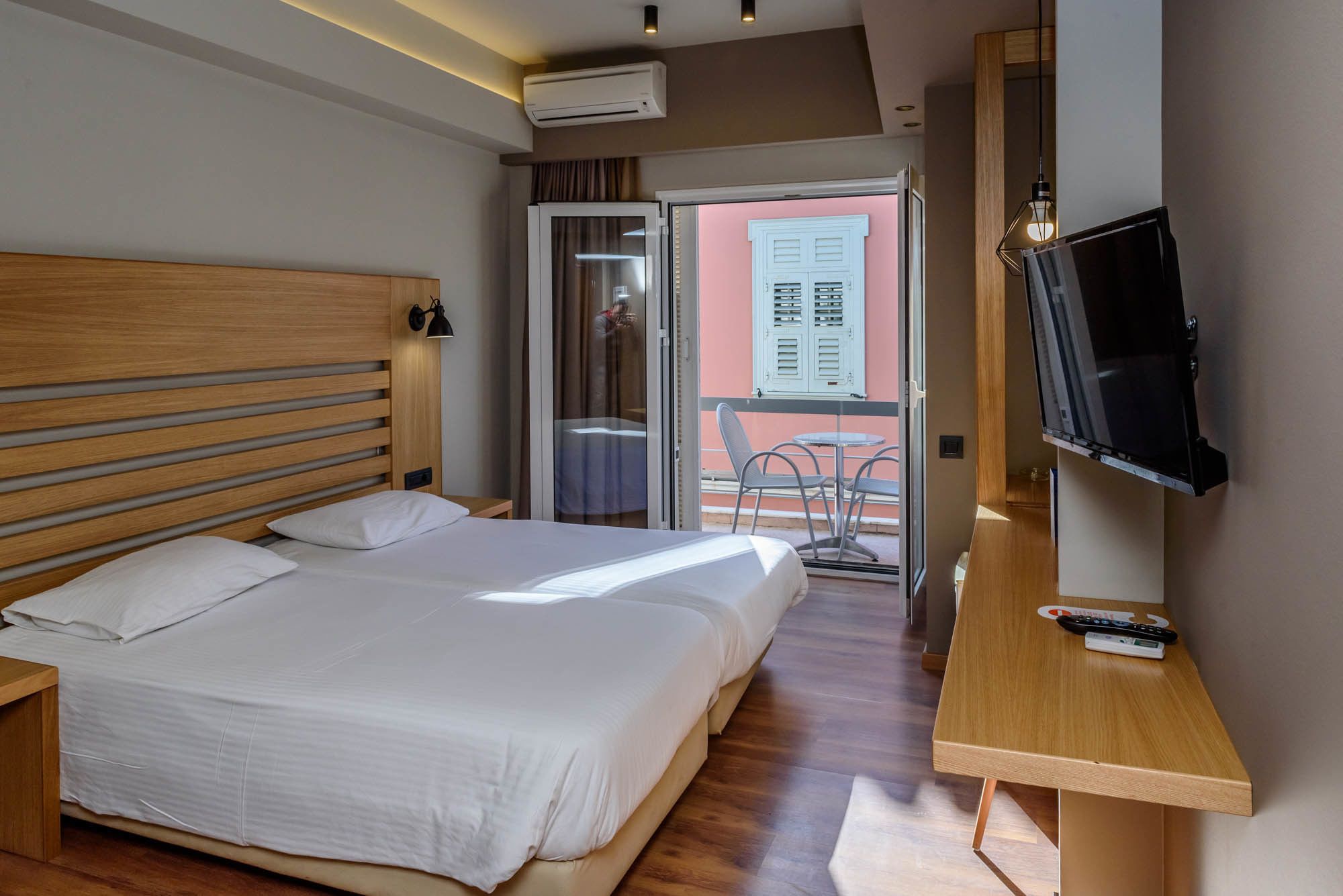 A hotel room with a large bed, a TV mounted on the wall, and a balcony with a table and chairs.
