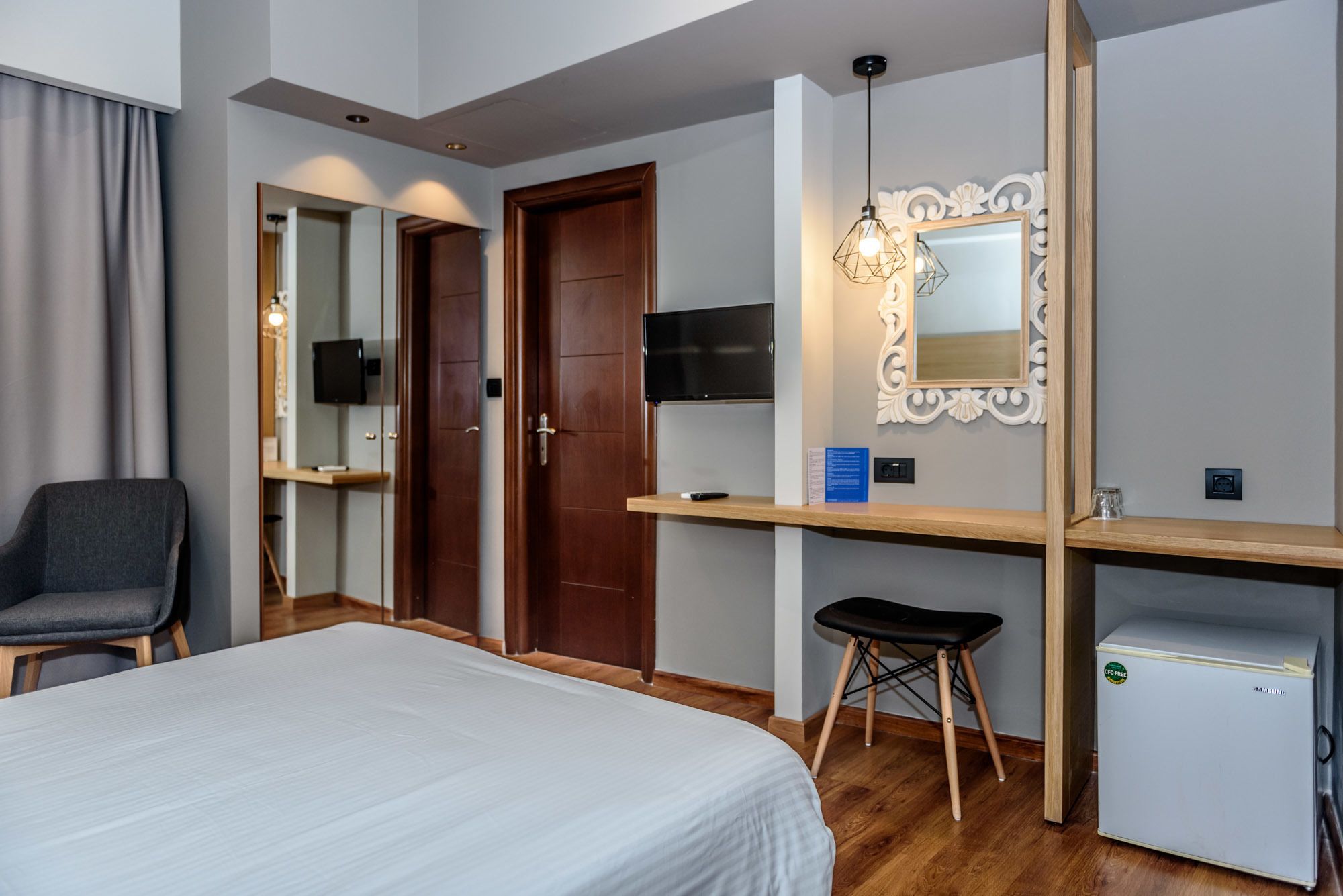 A hotel room with a bed, a desk with a computer, a chair, a TV, and a refrigerator.