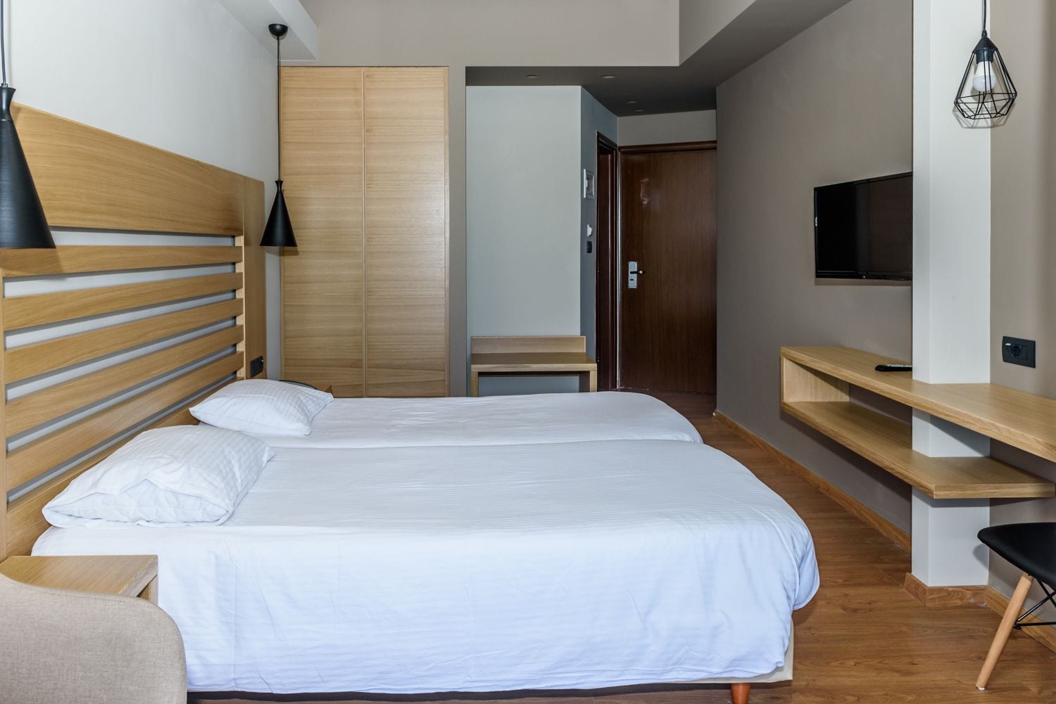 A hotel room with a double bed, wooden headboard, a TV, and a wooden wardrobe.
