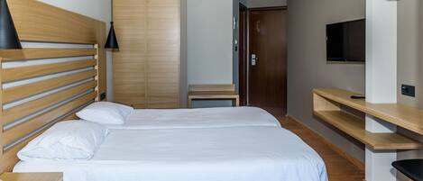 A hotel room with a double bed, wooden headboard, a TV, and a wooden wardrobe.