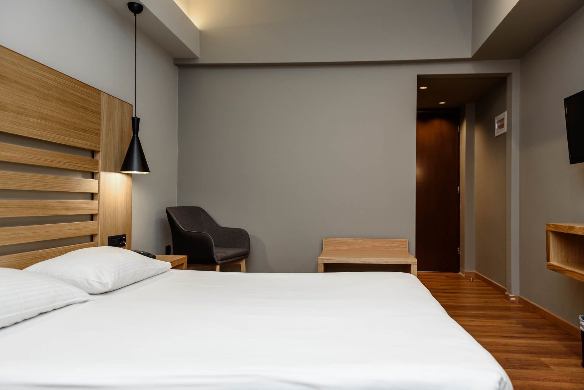 A modern hotel room with a large bed, a desk, a chair, and a small table.