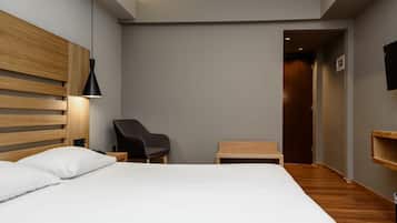A modern hotel room with a large bed, a desk, a chair, and a small table.