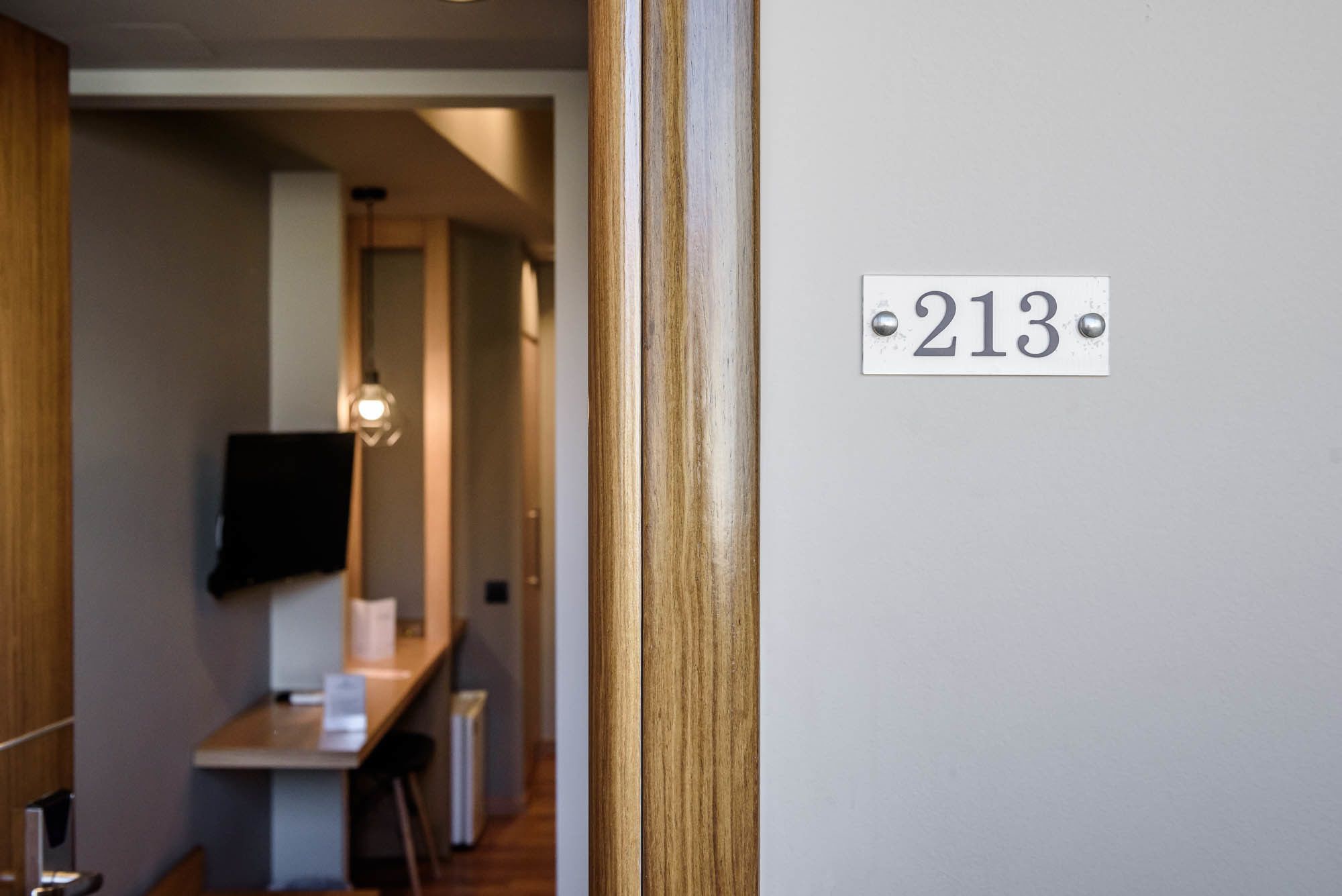A hallway with a number '213' on the wall, a wooden door frame, and a small table with a chair.