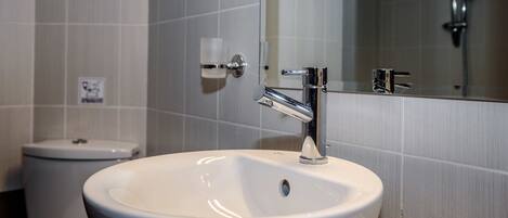 Une salle de bain avec un lavabo blanc, un robinet chromé et un miroir au-dessus.