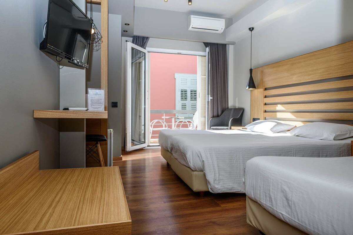 A hotel room with two beds, a TV, a desk, and a balcony with a view.