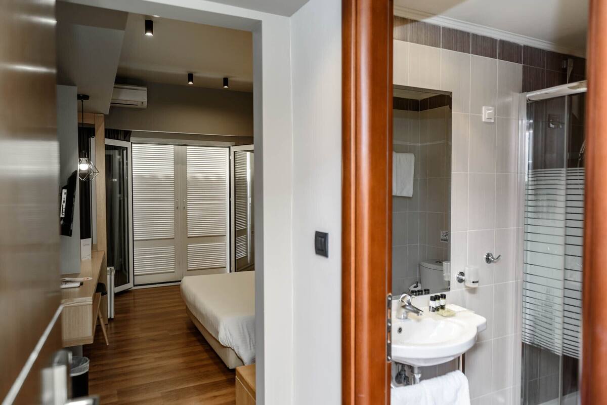 A hotel room with a bed, a desk, a mirror, a bathroom with a sink and toilet, and a shower.