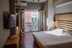 Habitación de hotel con cama, televisión, escritorio y balcón con sillas.