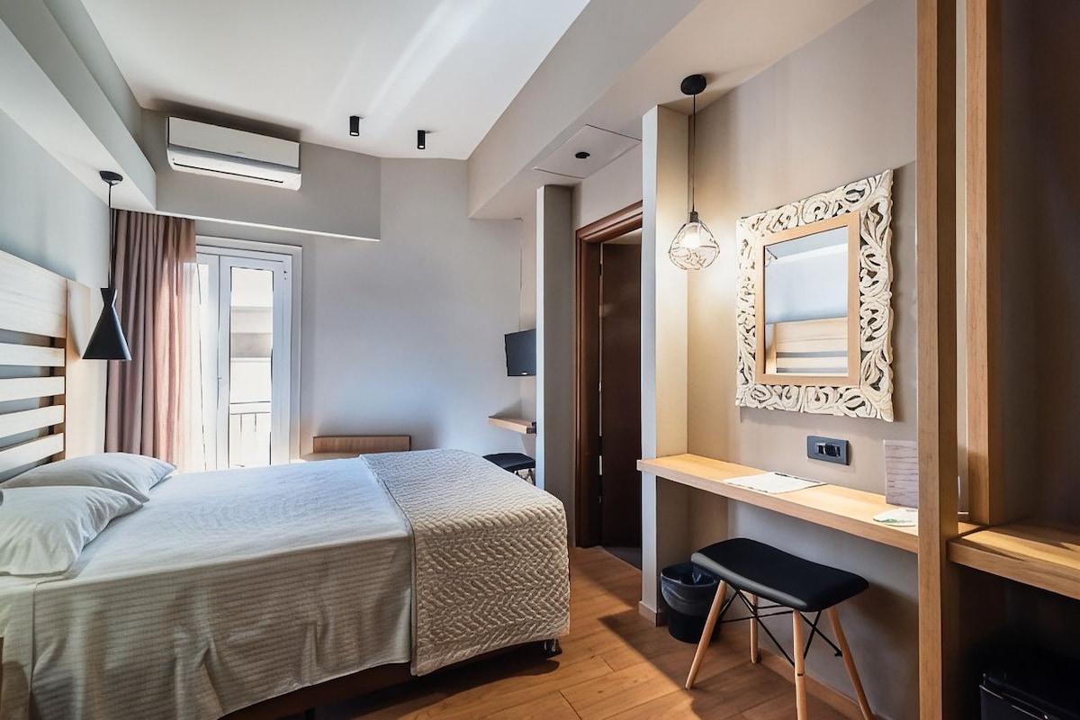 A hotel room with a bed, desk, chair, and a mirror with a decorative frame.