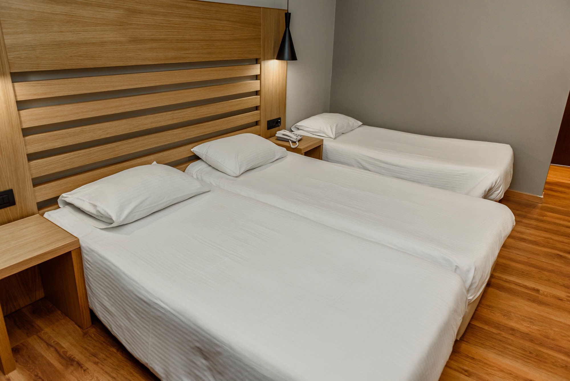 Quarto de hotel com cabeceira de madeira, duas camas de solteiro, mesa de cabeceira com telefone e criado-mudo.