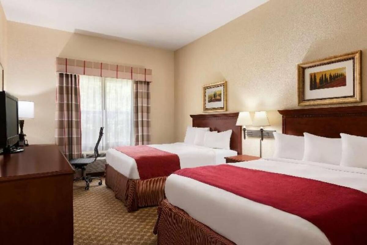 A hotel room with two beds, a desk, a chair, a television, and two framed pictures on the wall.
