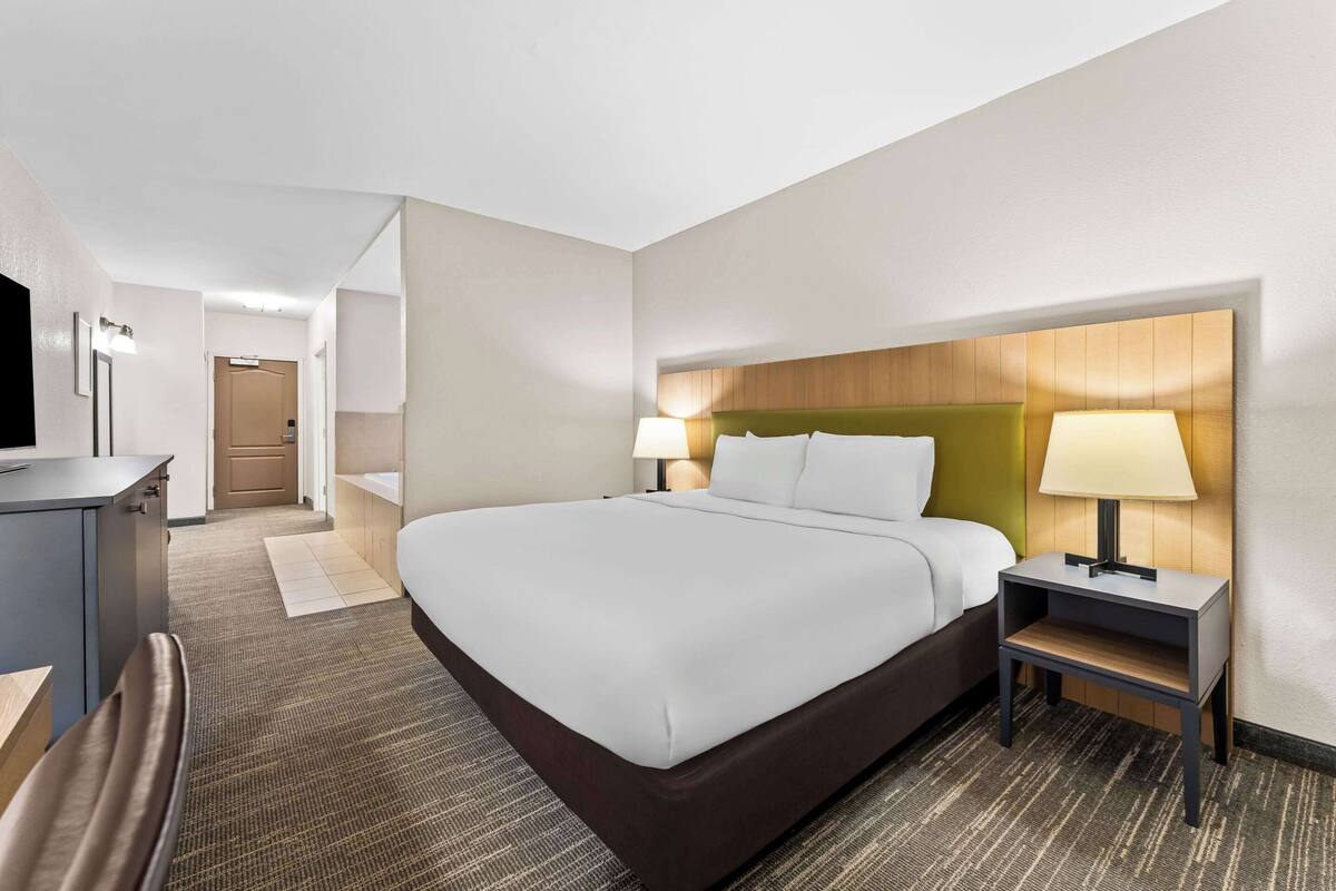 A hotel room with a large bed, bedside tables with lamps, a desk, and a television.