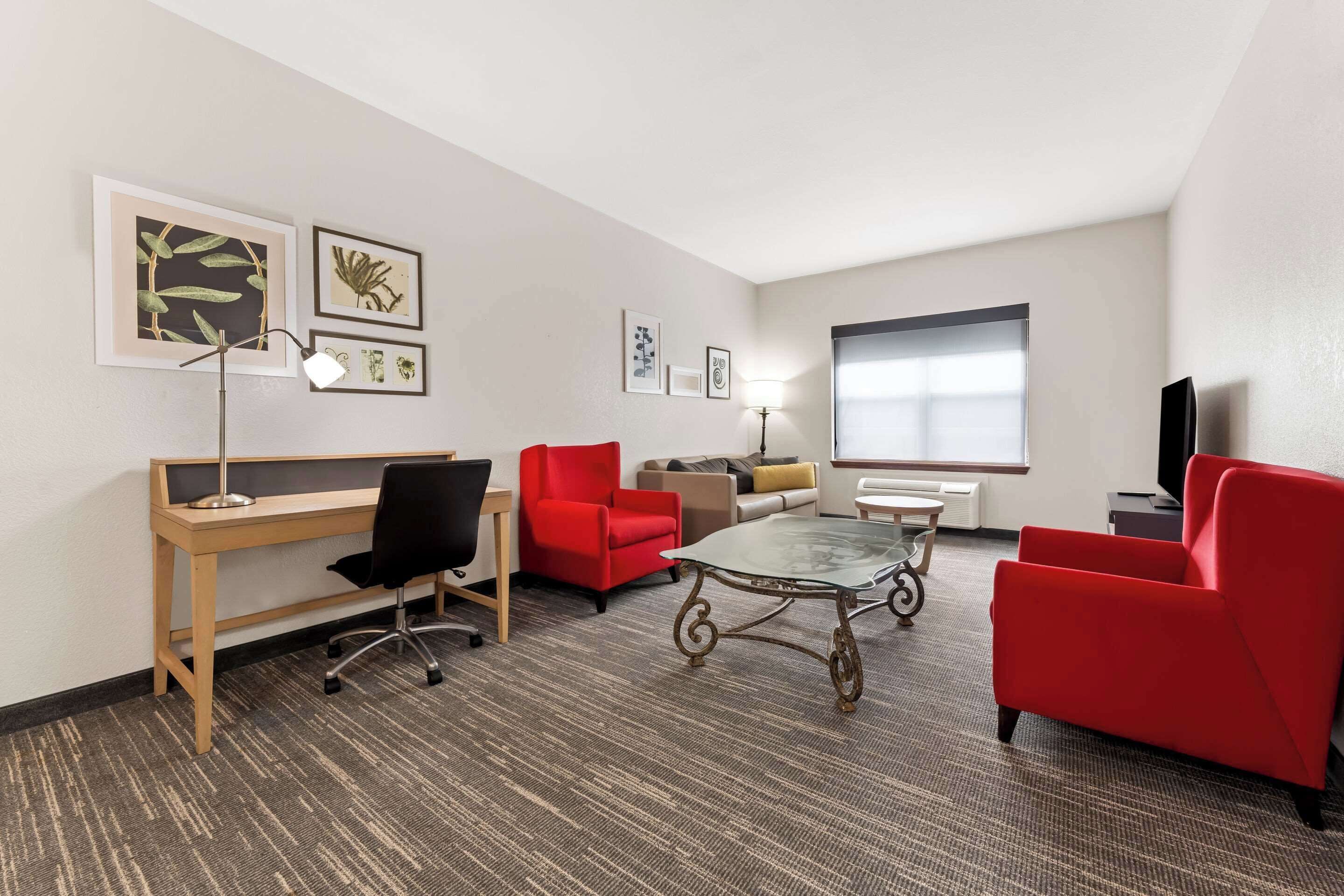A hotel room with a desk, two red chairs, a glass coffee table, and a TV.