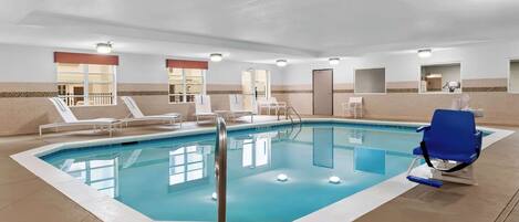 An indoor swimming pool with clear water, surrounded by lounge chairs and a blue chair.