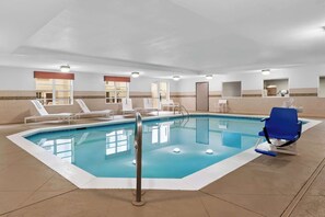 An indoor swimming pool with clear water, surrounded by lounge chairs and a blue chair.