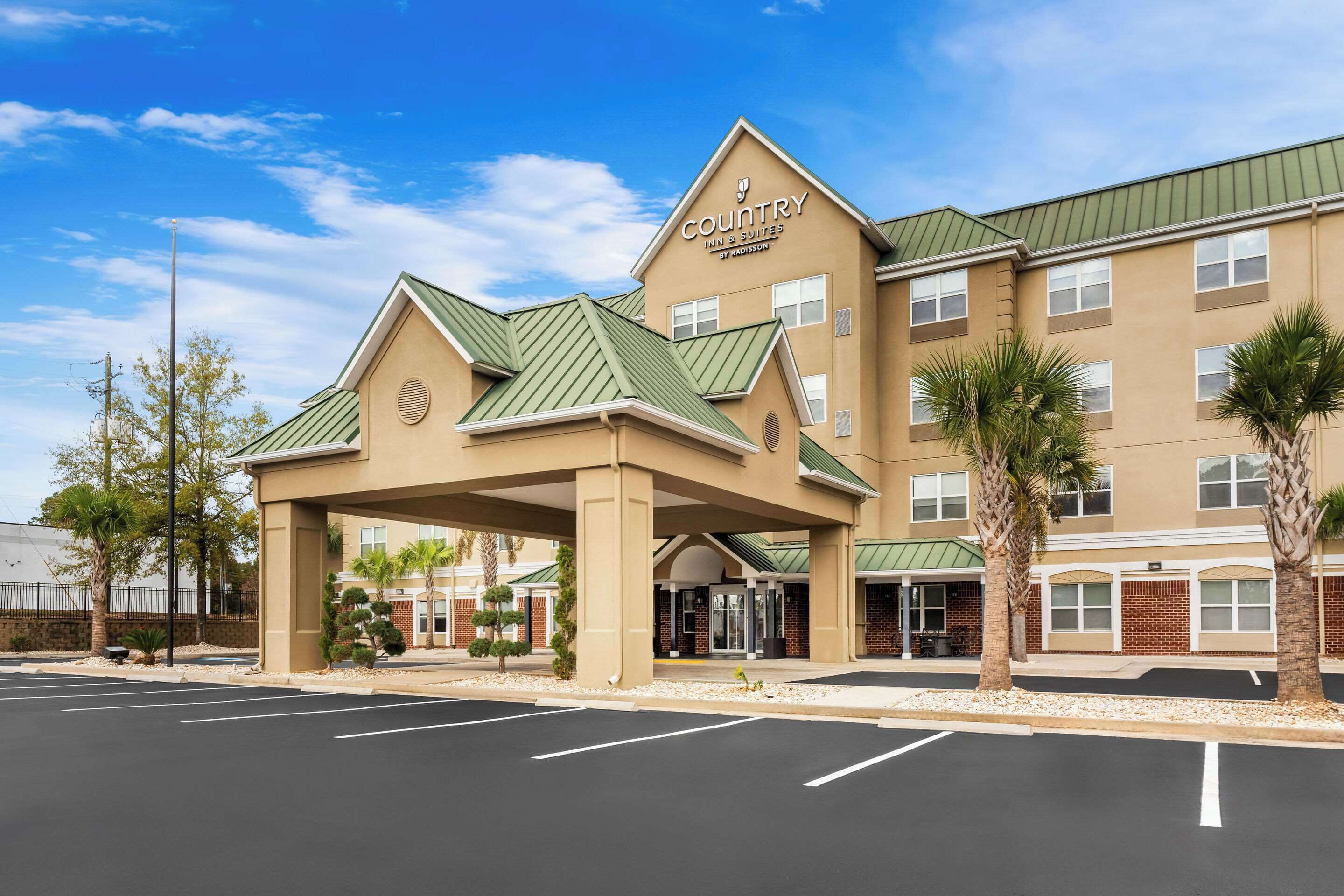 A Country Inn & Suites building with a green roof, a covered entrance, and a parking lot.