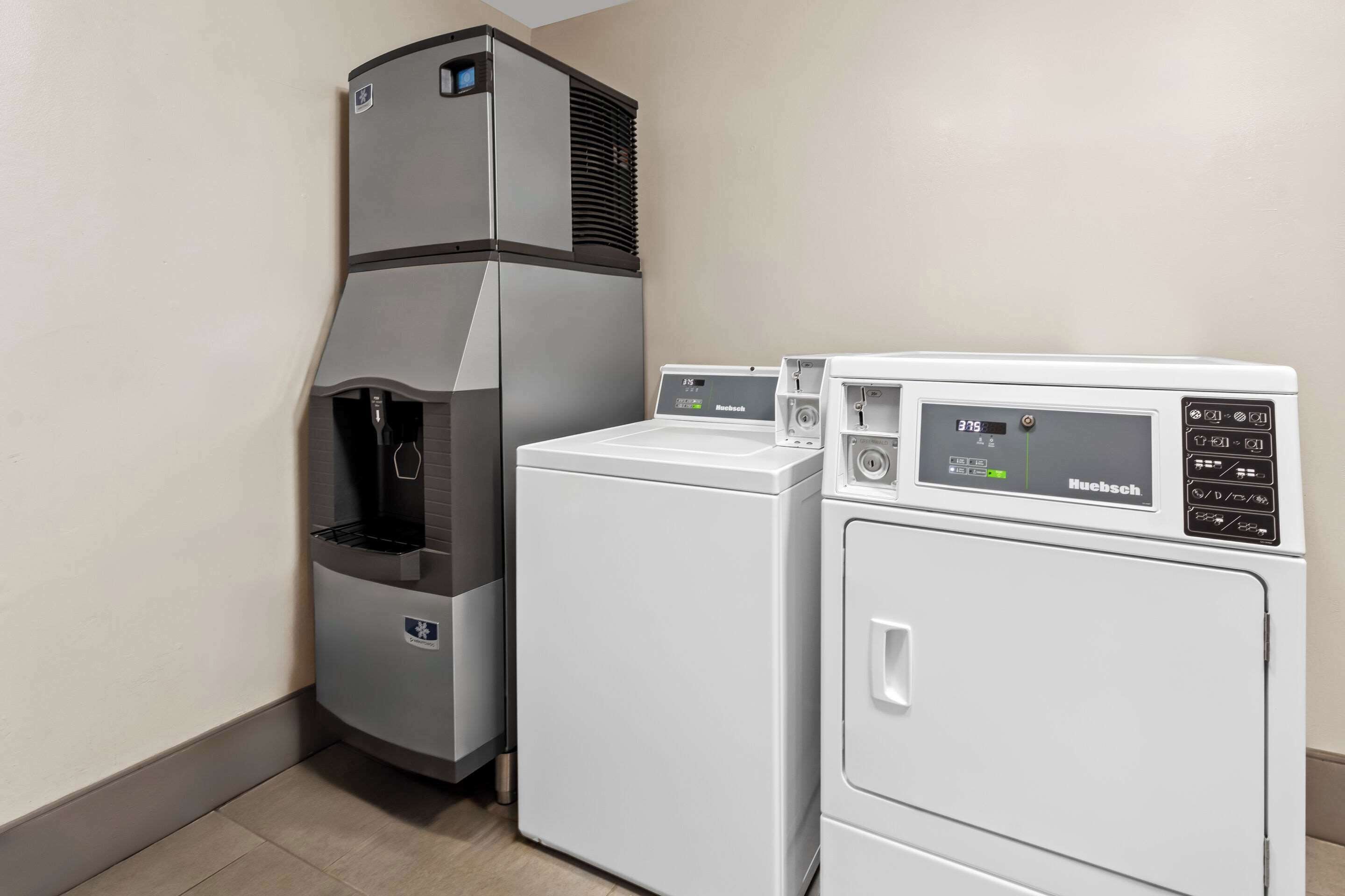A compact laundry area with a high-efficiency washer and dryer, a water dispenser, and a control panel.