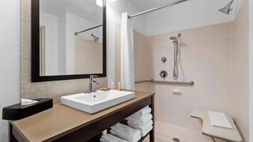 Un baño moderno con un espejo grande, un lavamanos, ducha con barras de apoyo y un perchero para toallas.