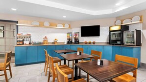 Een moderne keuken met blauwe kastjes, houten tafels en een flatscreen televisie aan de muur.