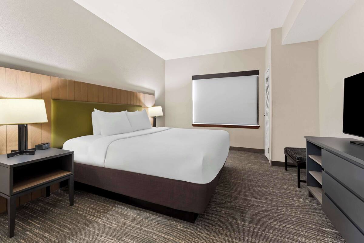 A hotel room with a bed, bedside tables, a desk, a chair, a television, and a large window.
