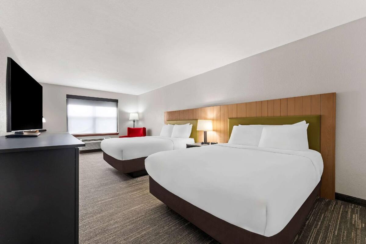A hotel room with two beds, a desk with a TV, and a window with blinds.
