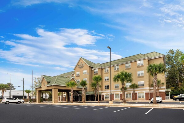 A hotel with a green roof, multiple floors, and a covered entrance area with palm trees.