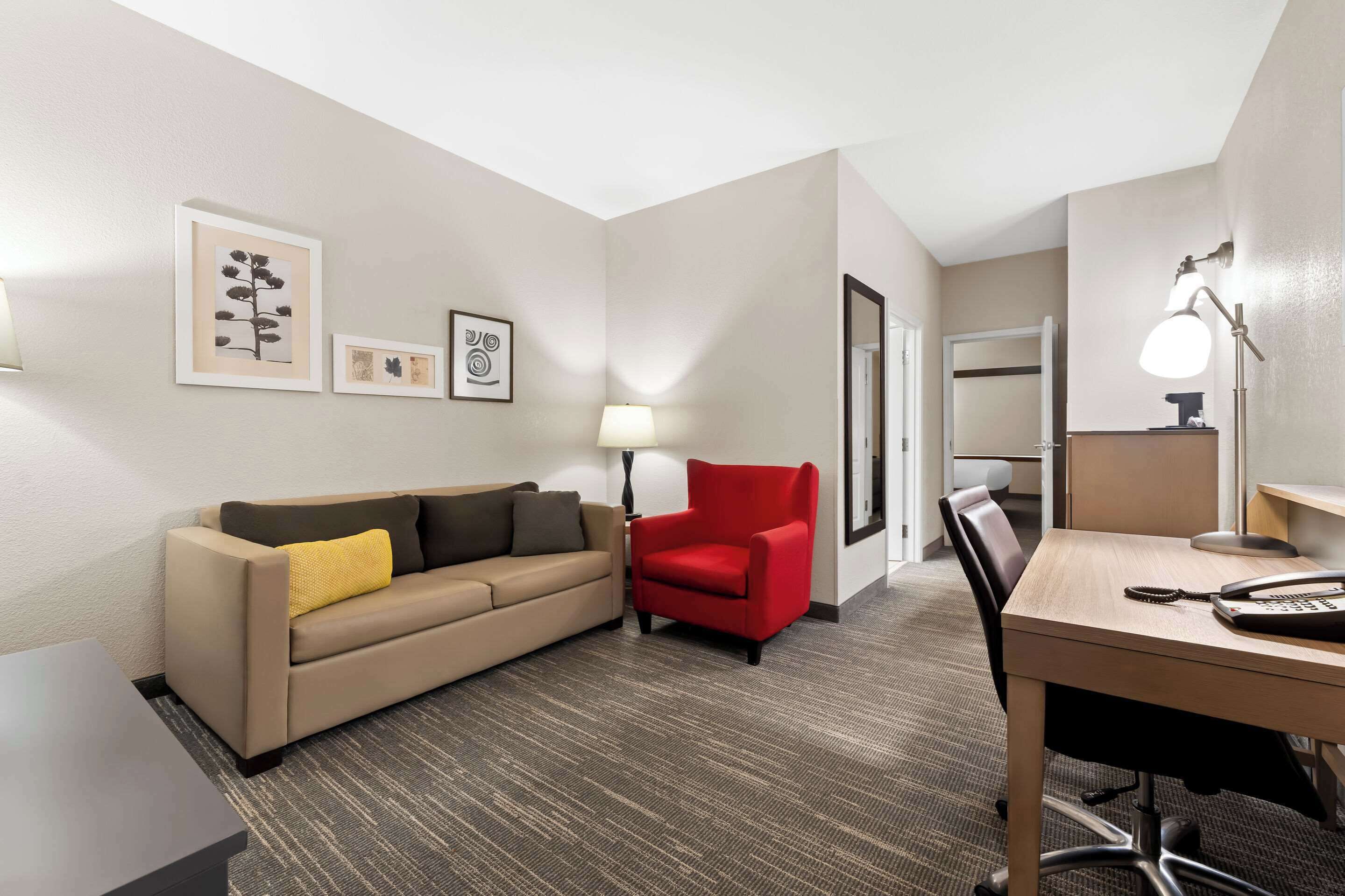 A hotel room with a sofa, a red armchair, a desk with a telephone, and framed artwork on the wall.