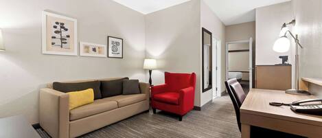 Une chambre d’hôtel avec un canapé, un fauteuil rouge, un bureau avec un téléphone et des œuvres d’art encadrées accrochées au mur.