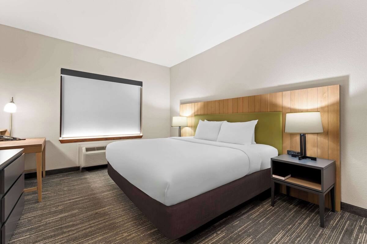A hotel room with a large bed, two bedside tables with lamps, a desk, and a large window.